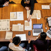 Overhead shot of rare documents spread out on wood table with students and professors and laptops surrounding them. 