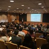 an audience listening to a presentation in a lecture hall by a speaker at the front of the room