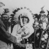 Man shakes hands with member of Ojibwe tribe of Wisconsin, an another man in headdress looks on.