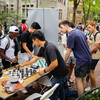 students playing chess outside on a table with several others watching