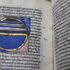 Open pages of John Trevisa book with ancient language and a round blue symbol among the text.