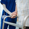 A health care professional with a person walking with a walker.