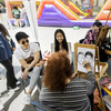 Two students sitting for a caricature drawing at the annual Spring Porch Party. An artist is drawing their picture. Both students are smiling.