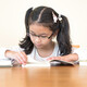 A child sits at a table reading a book, two closed books are on the table beside them.