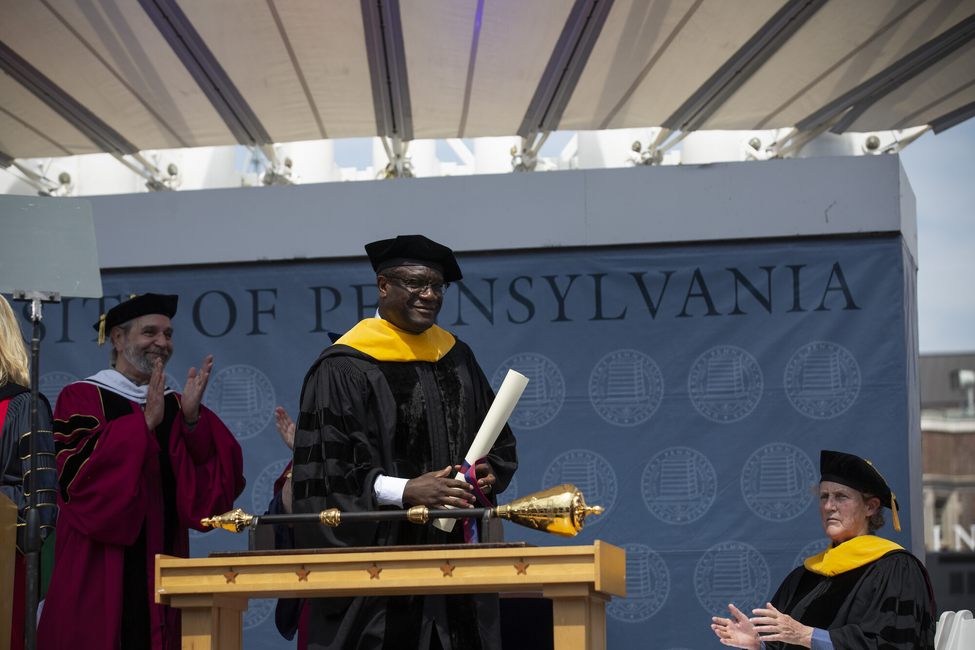 Michael Delli Carpini claps as Denis Mukwege holds his honorary degree, with Temple Grandin seated and clapping.