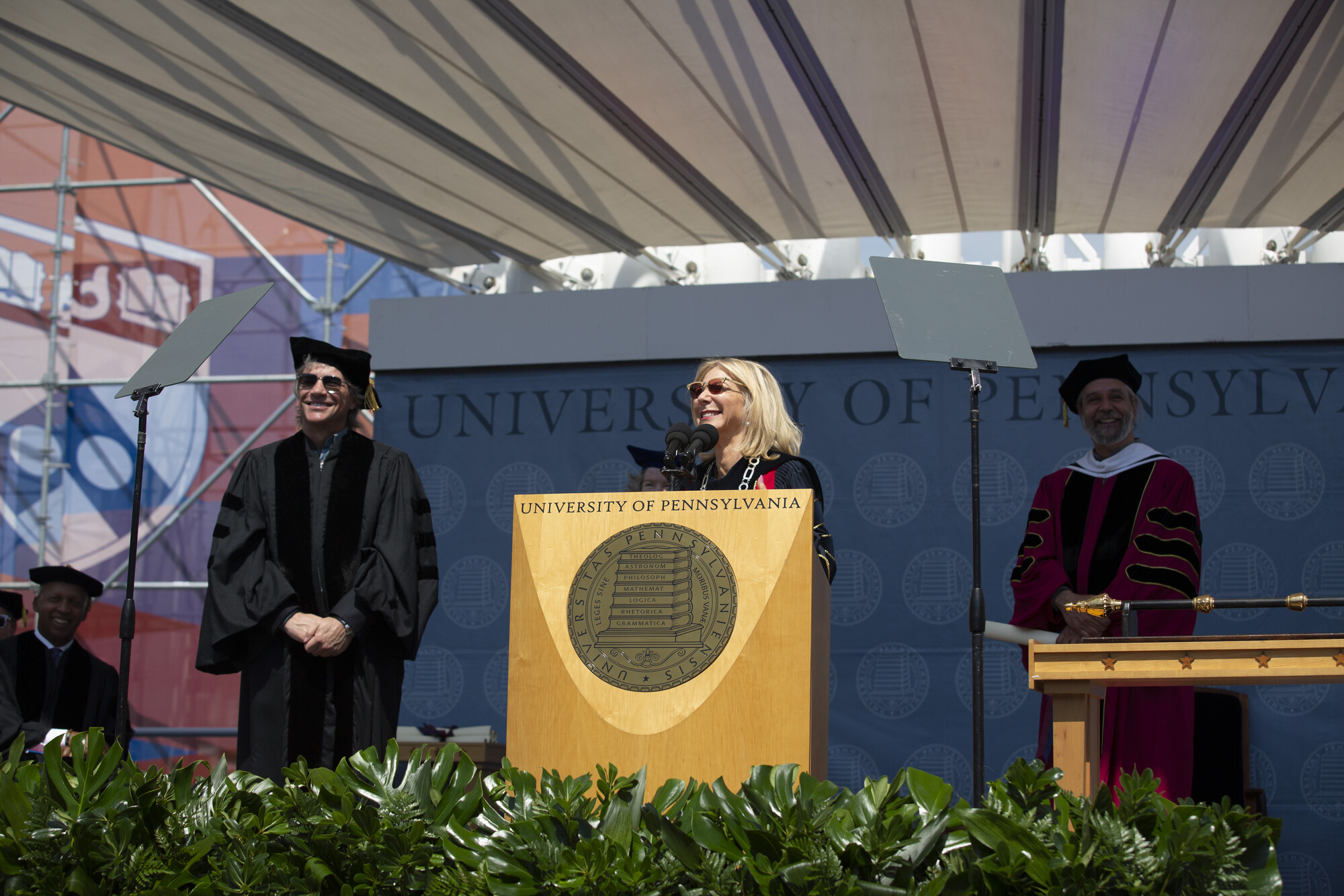Jon Bon Jovi, Amy Gutmann and Michael Delli Carpini on stage during commencement, Gutmann is at a podium.