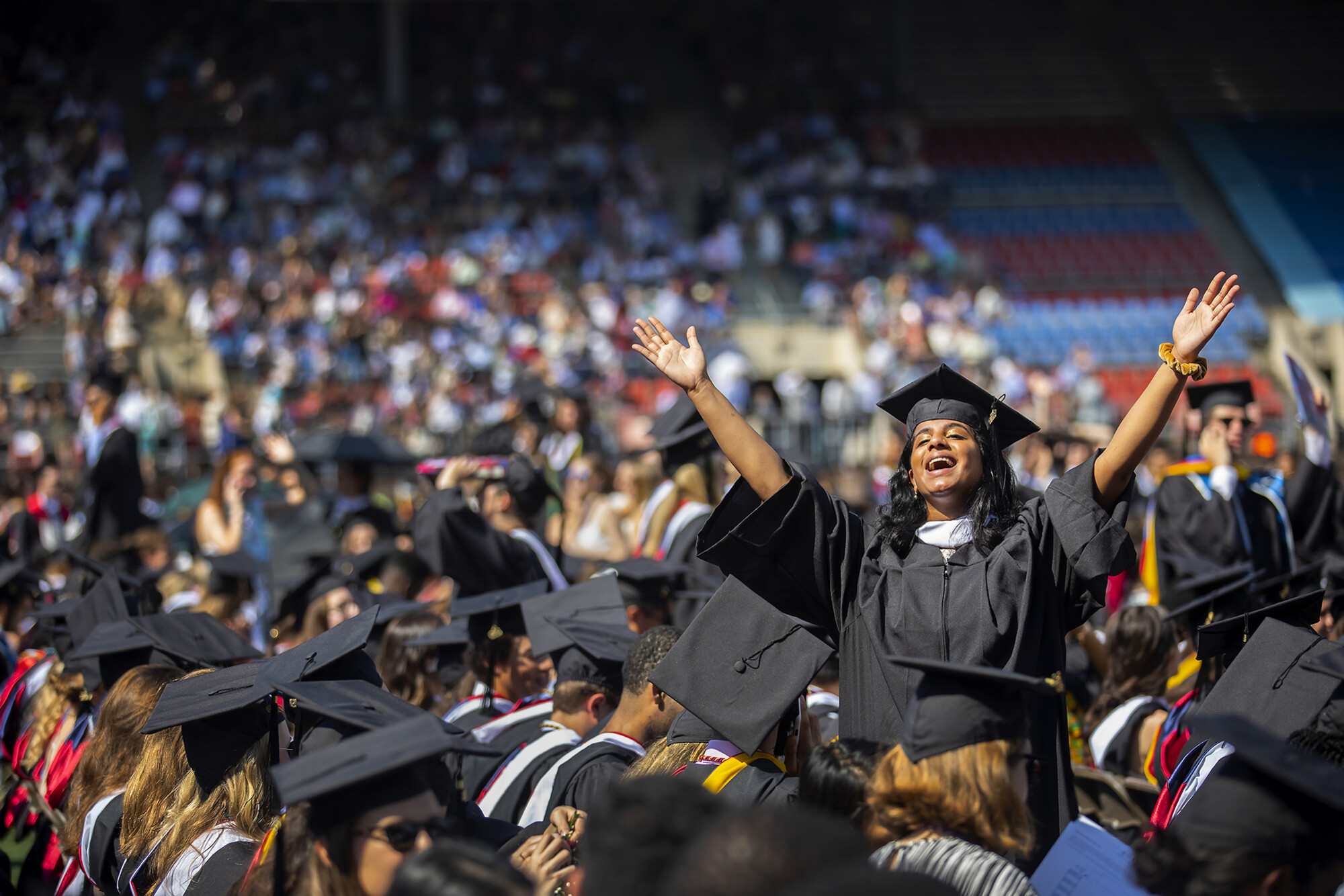 One graduate stands amidst seated graduates in celebration.