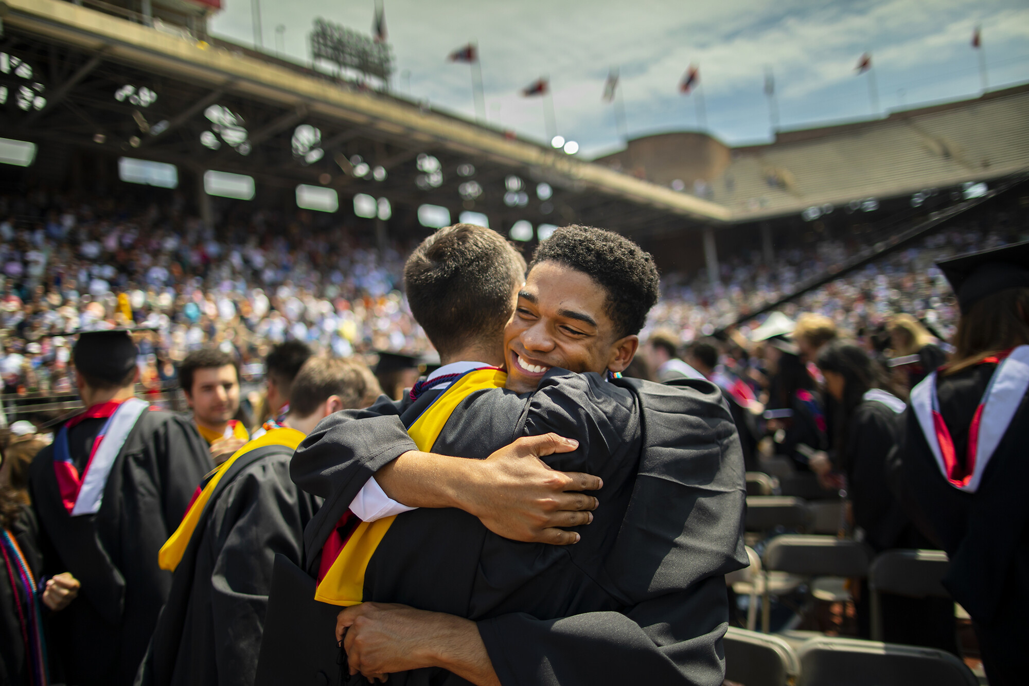Two graduates embrace on the field at commencement.
