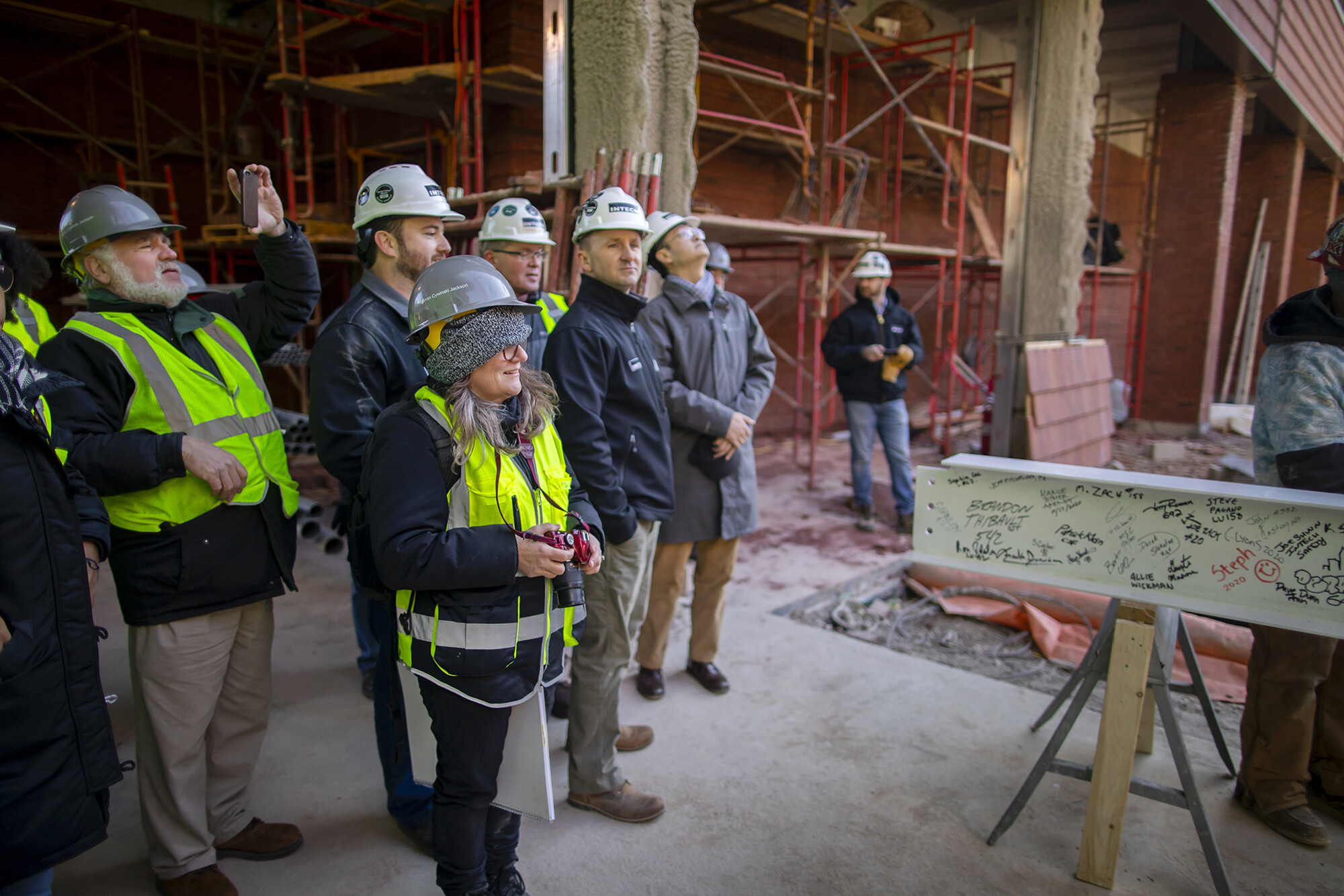 A group of people involved with the New College House West construction, including the architect on the far left, stand before the final beam before it is lifted in place. 