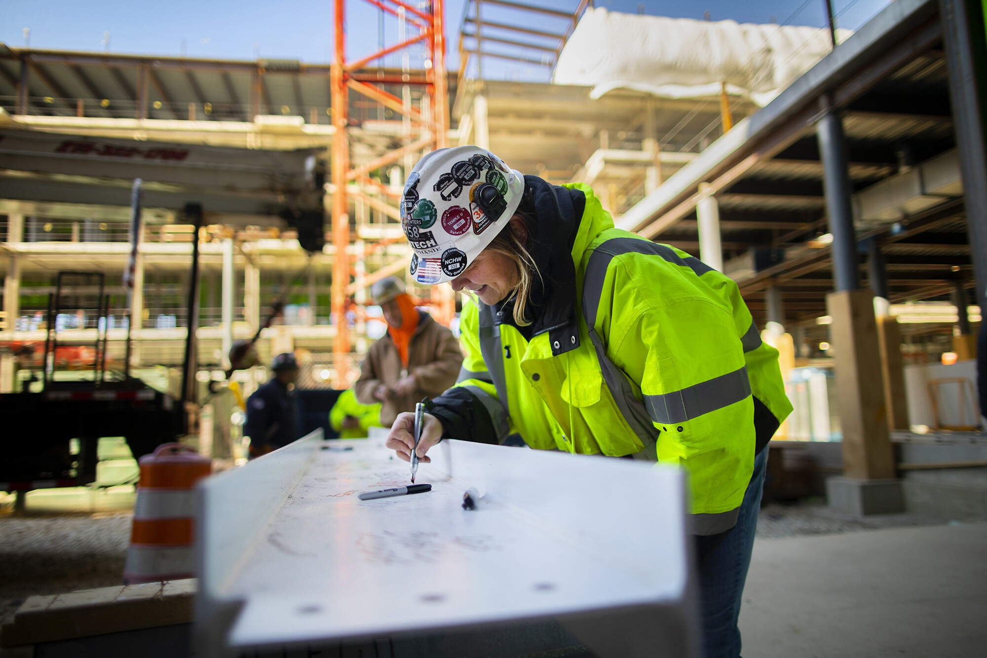 A worker in a hard hat smiles and signs the final beam with a Sharpie