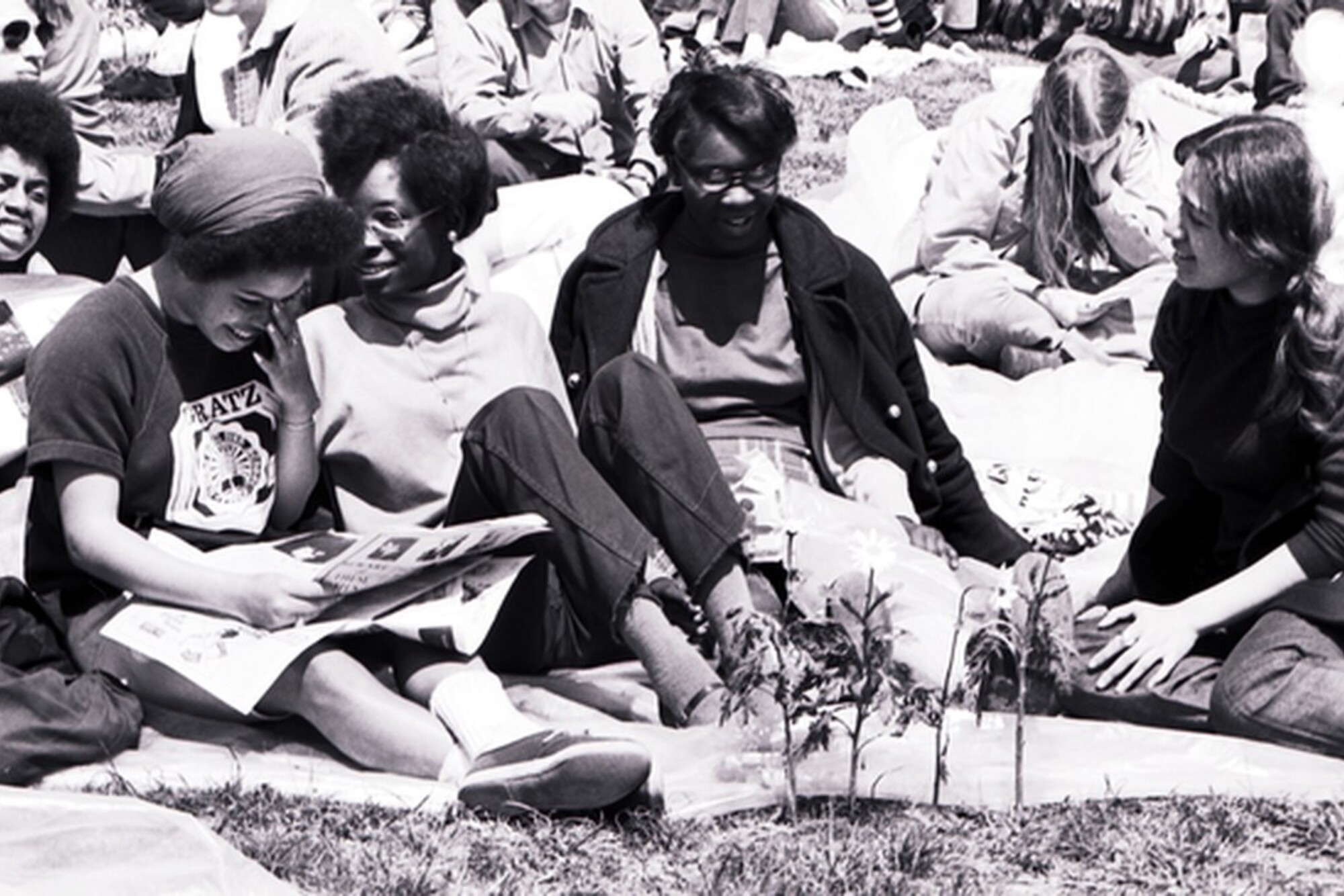 Four people sit on blankets on the grass, smiling.