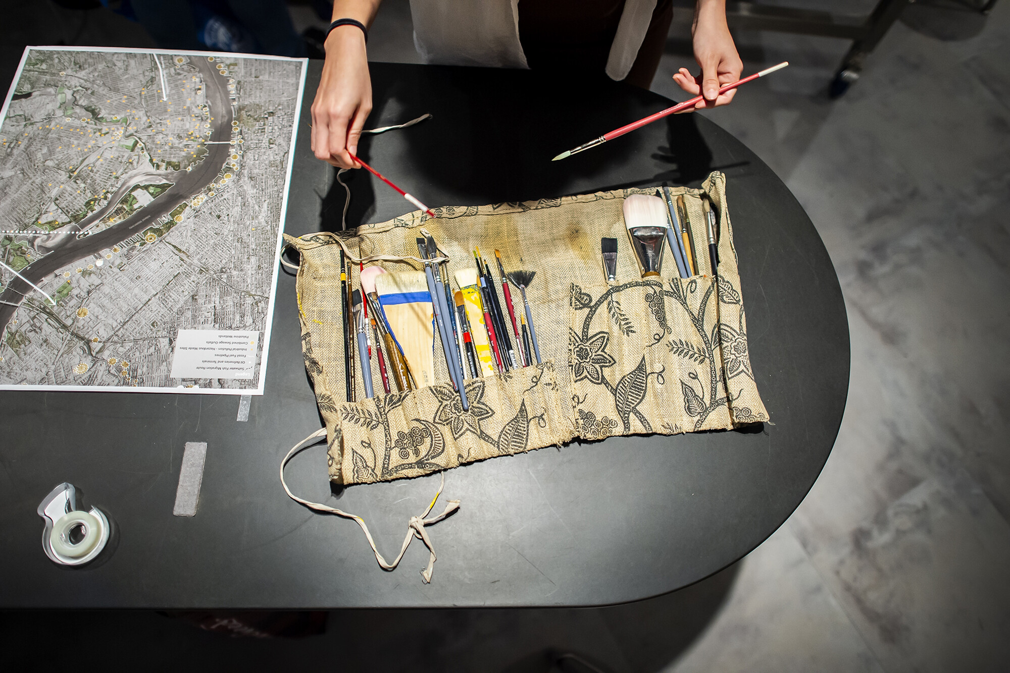 Overhead view of paintbrushes in a fabric kit and a satellite map.