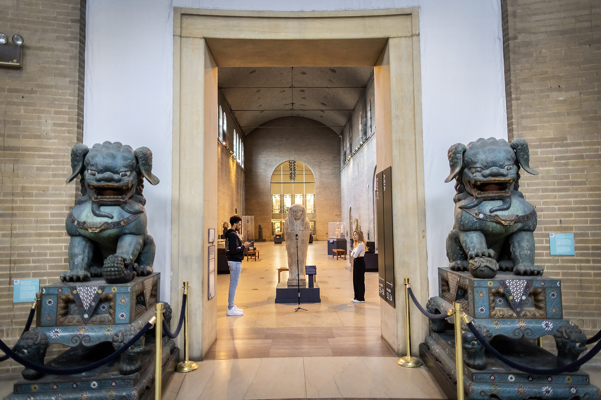 Two members of the VR class curator group standing in the Egyptian wing by an entrance with two identical statues.