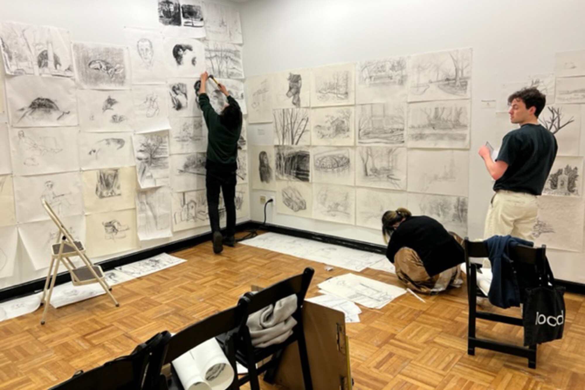 Students hang their drawings on the wall of a gallery.