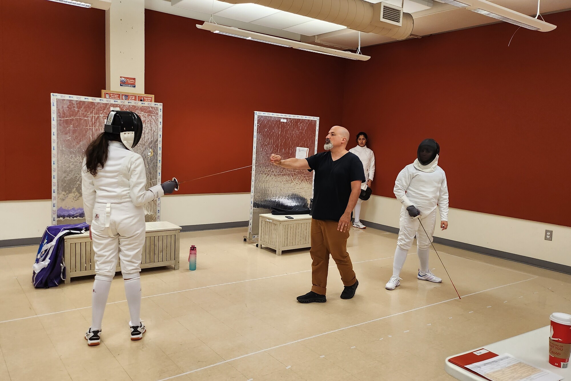 A fencing instructor directs three actors in fencing gear during play rehearsal.