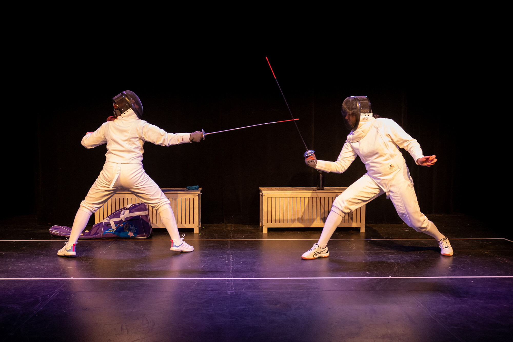 Two actors in fencing gear performing on stage.