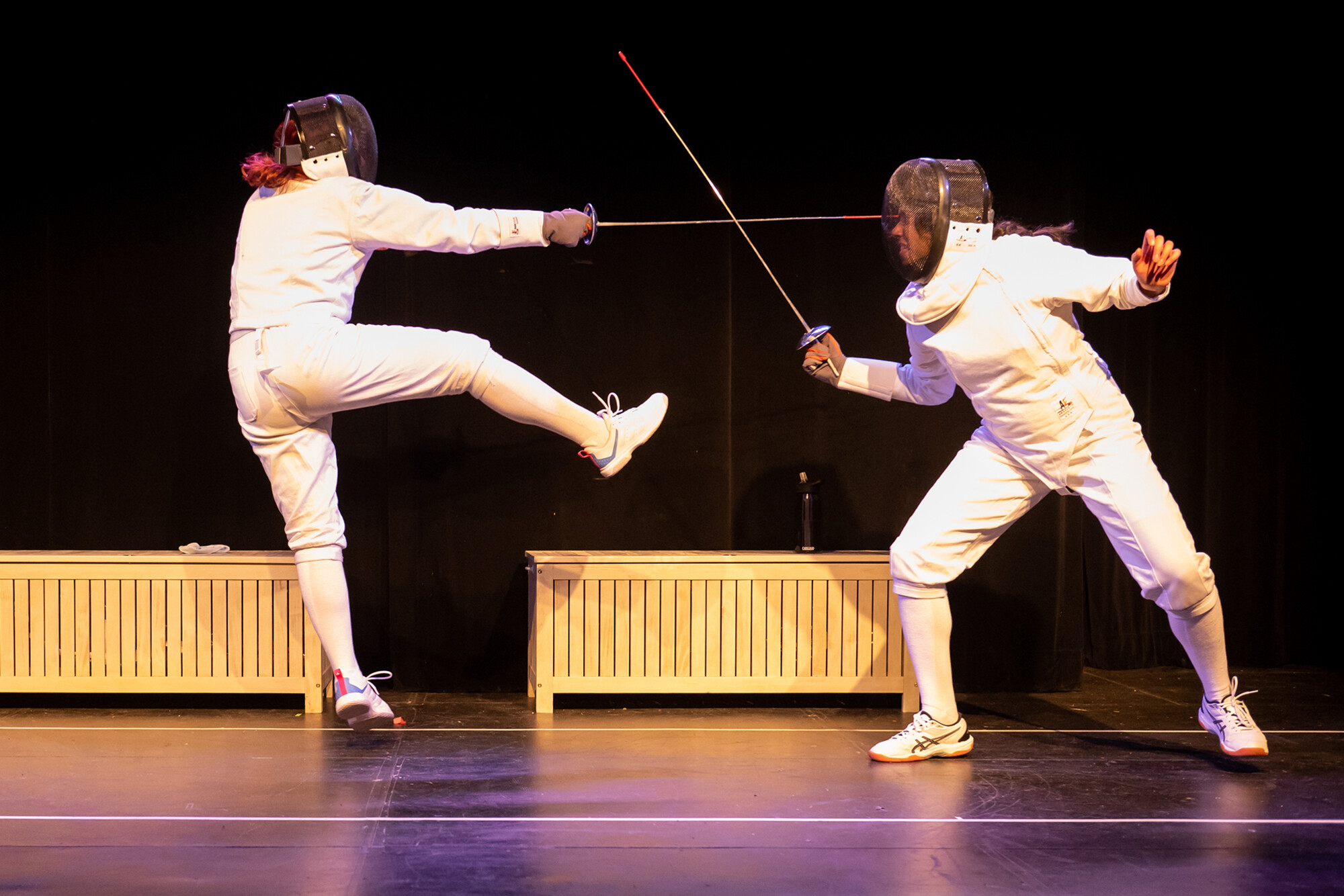 Two actors in fencing gear performing on stage.