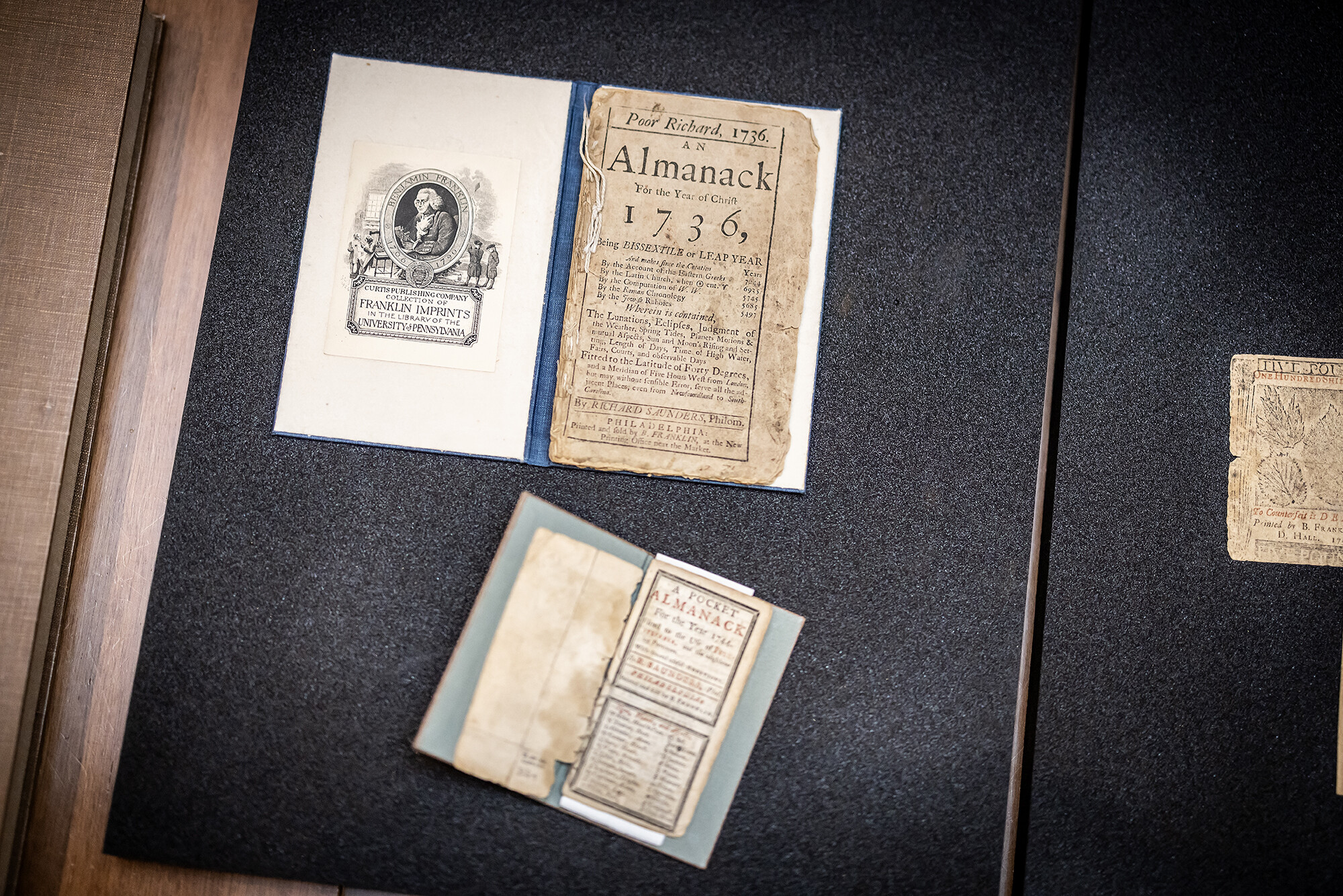 Two historic Almanacs from the 1700s and a piece of currency Ben Franklin printed.