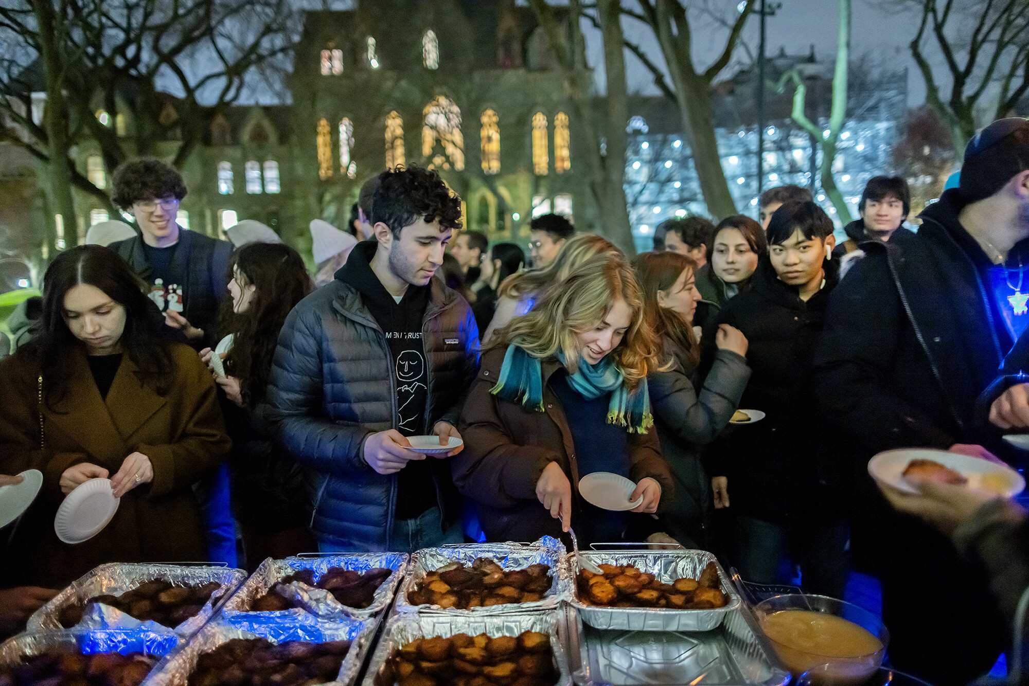 People serving themselves food at a Hanukkah gathering in front of College Hall.
