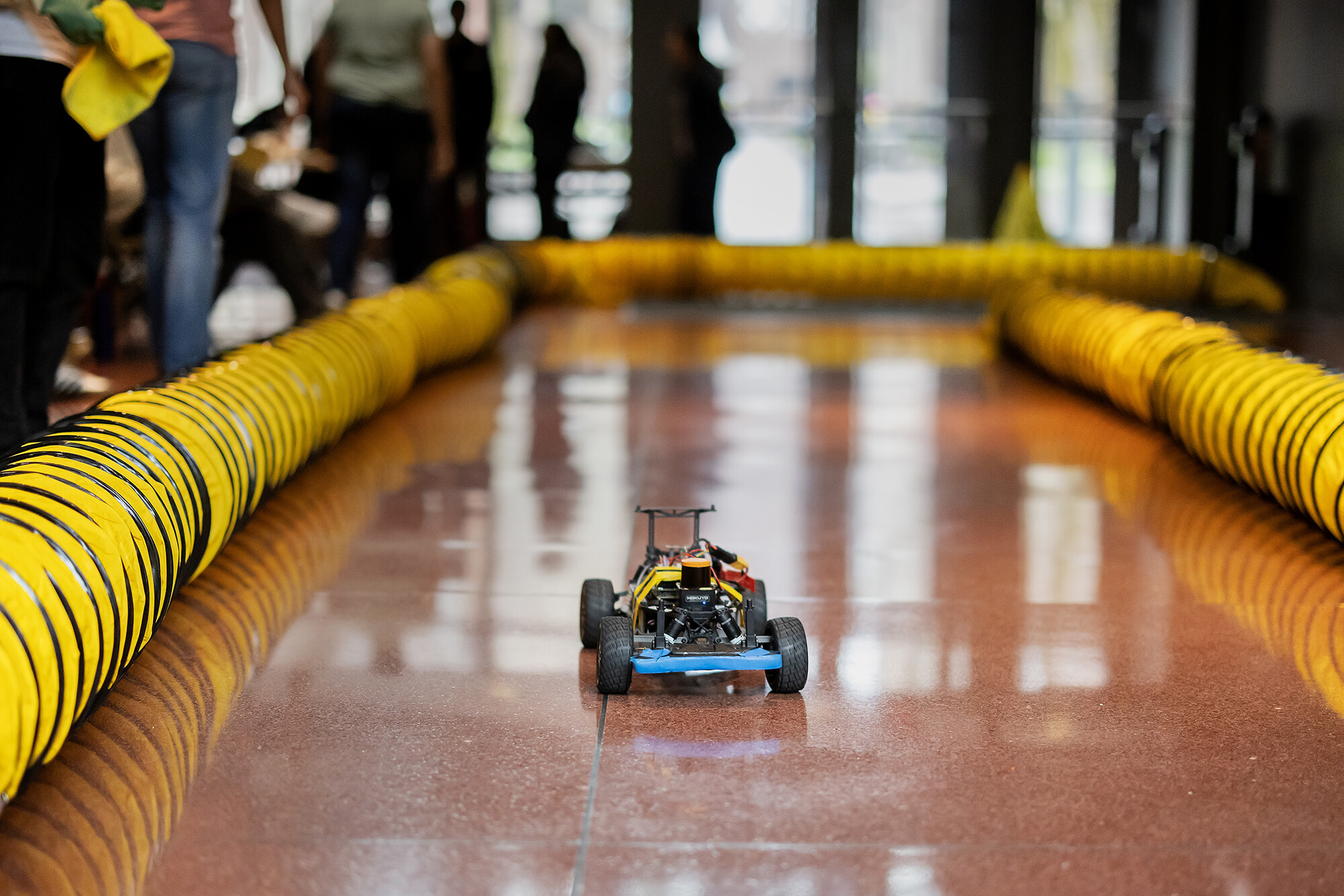 A small racecar in a makeshift track in Penn Engineering with student spectators.