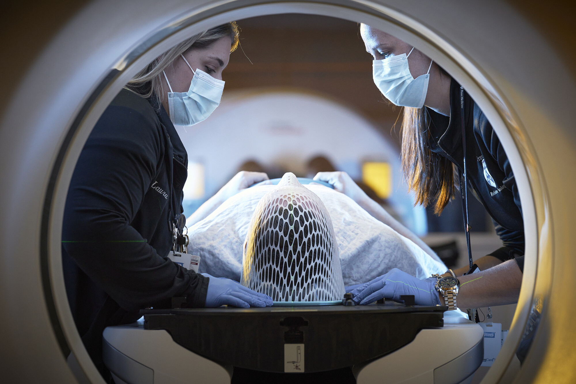 Two nurses guiding a prone patient into a proton imaging machine.
