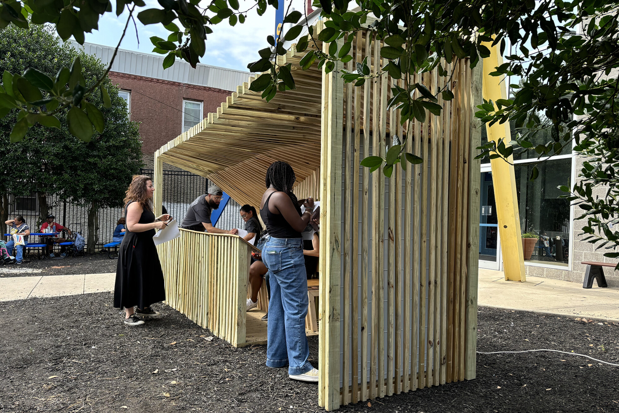 Sara Jacoby and others outside a wooden cooling shelter protoype in a Philly neighborhood.