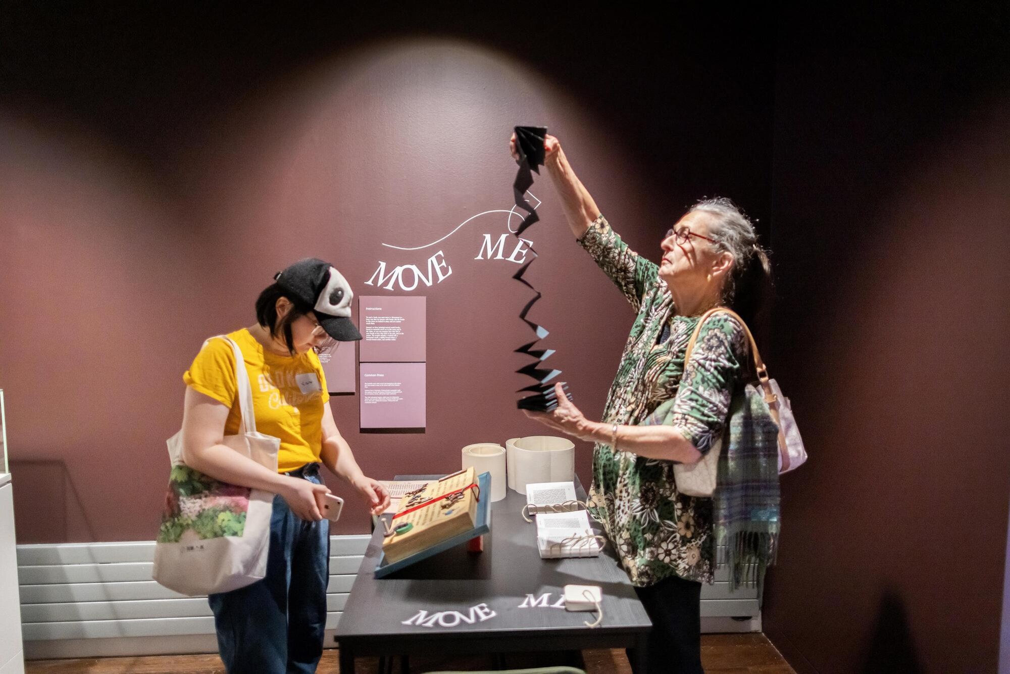 Two people looking at books at the exhibit, one holds up a folding book.