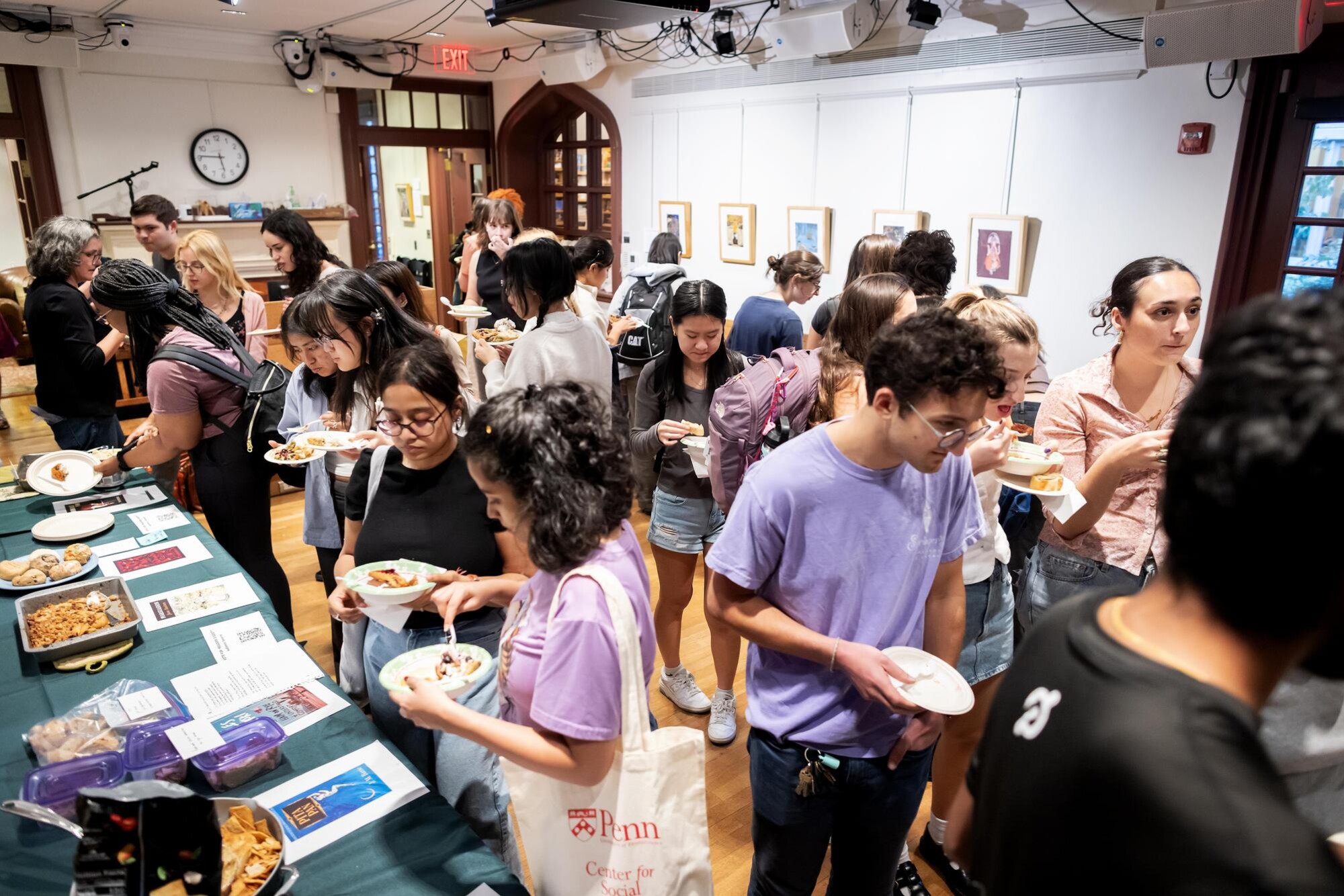 A crowded room with people eating food on plates as they look at the displays of food art based on books.