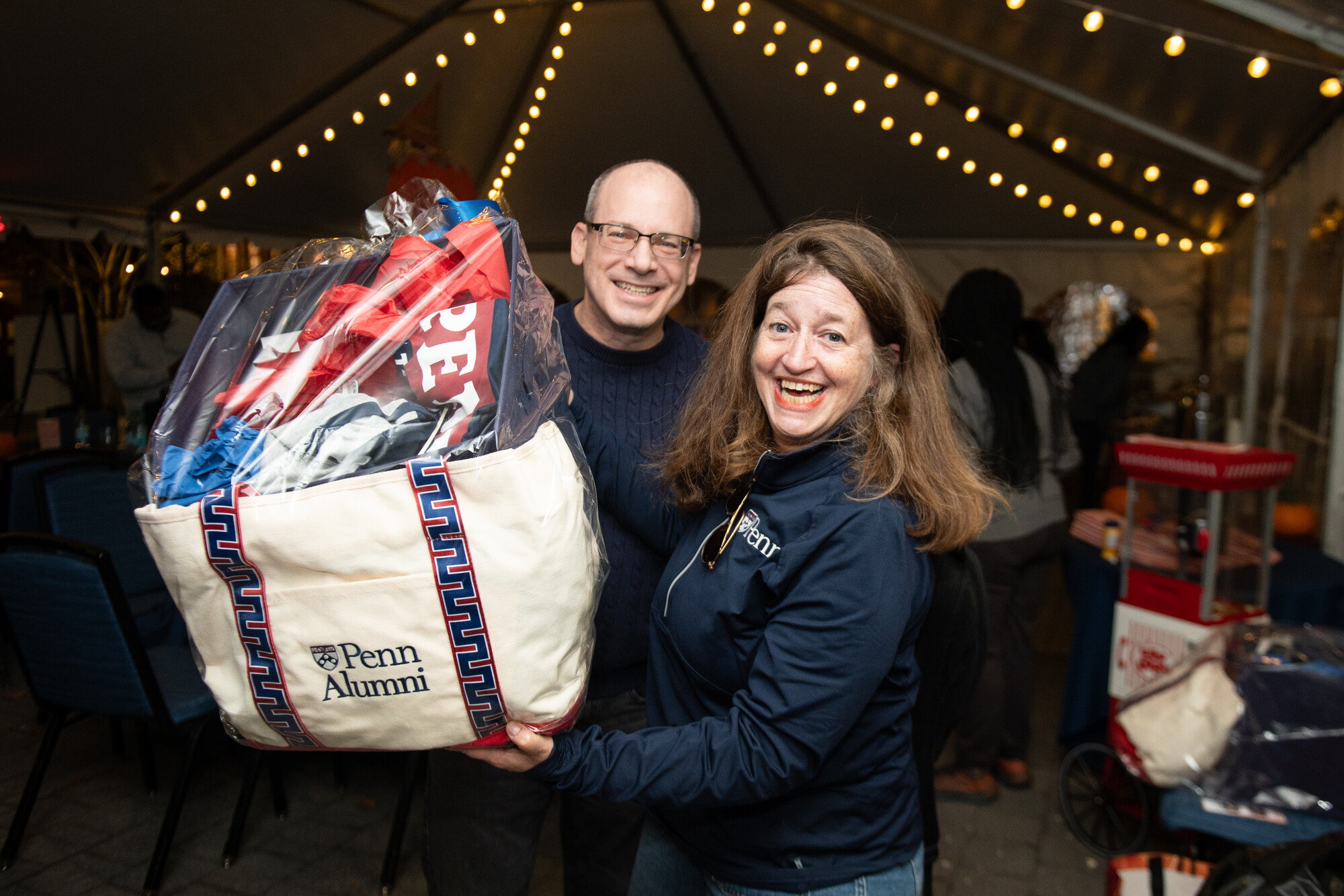 Two Penn alums on Penn’s campus holding a bag full of Penn swag during Friends and Family Weekend.