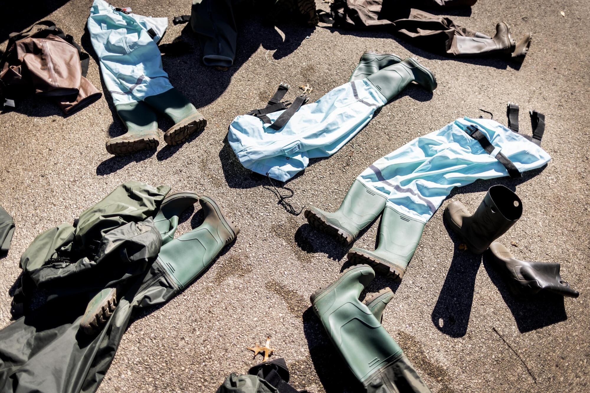 Waders and boots in a pile on the ground.