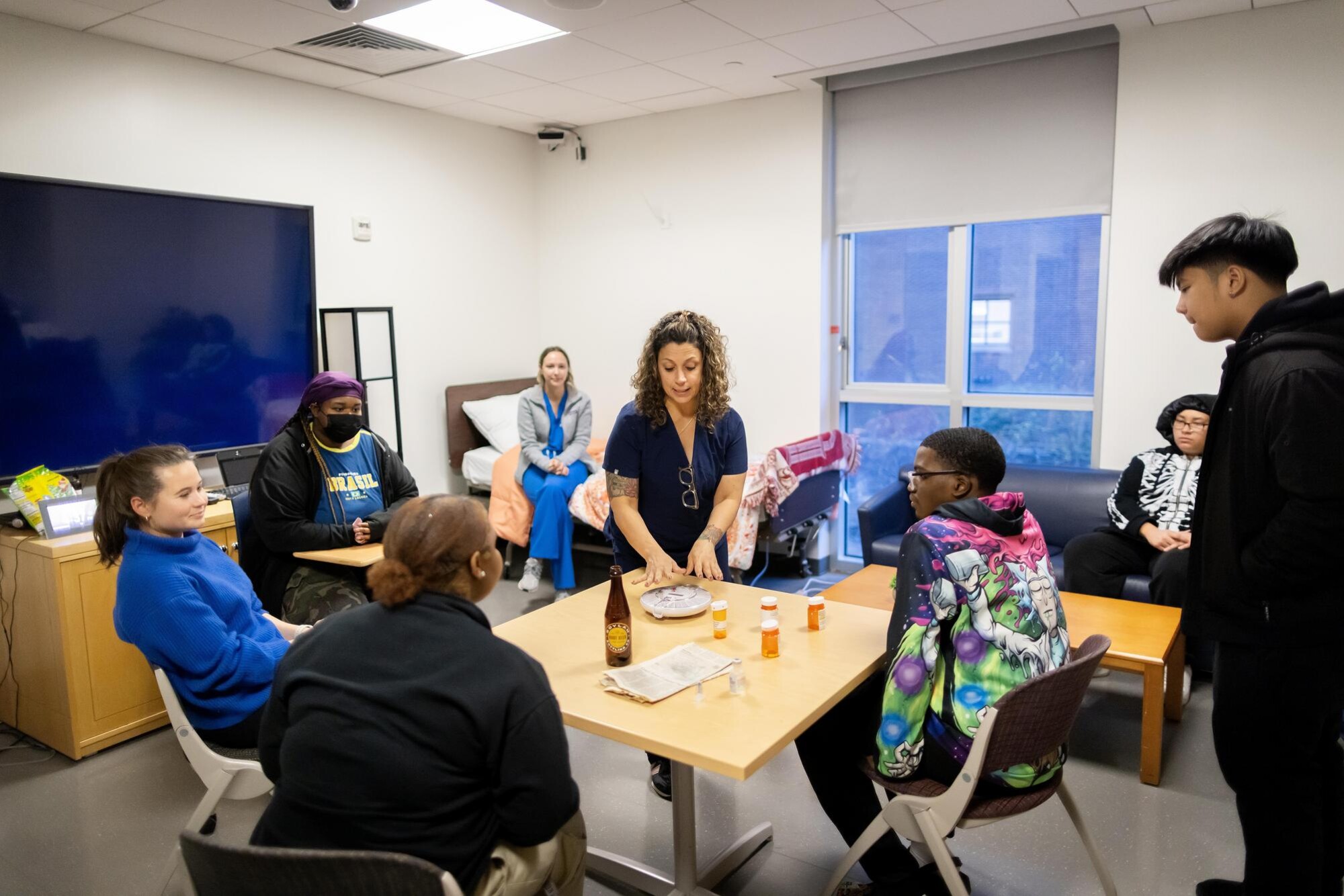 A Penn Nursing student lectures high school students seated at a table.