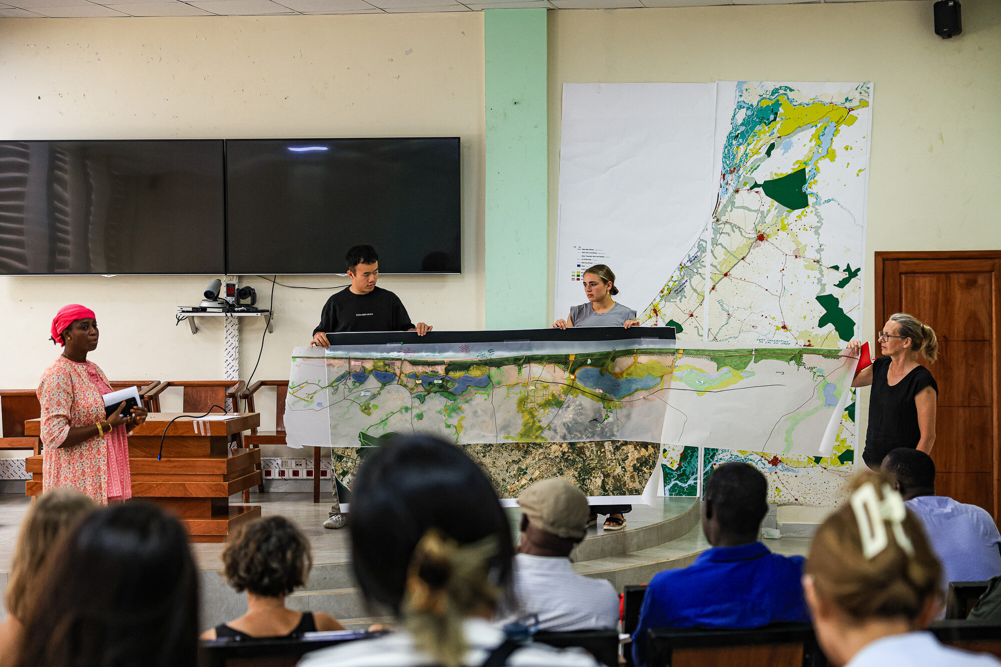 A group of people presents a large-scale map in a lecture setting. 