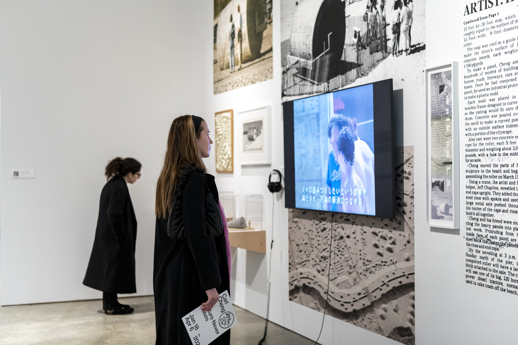 two people looking at a wall with photos and a video screen