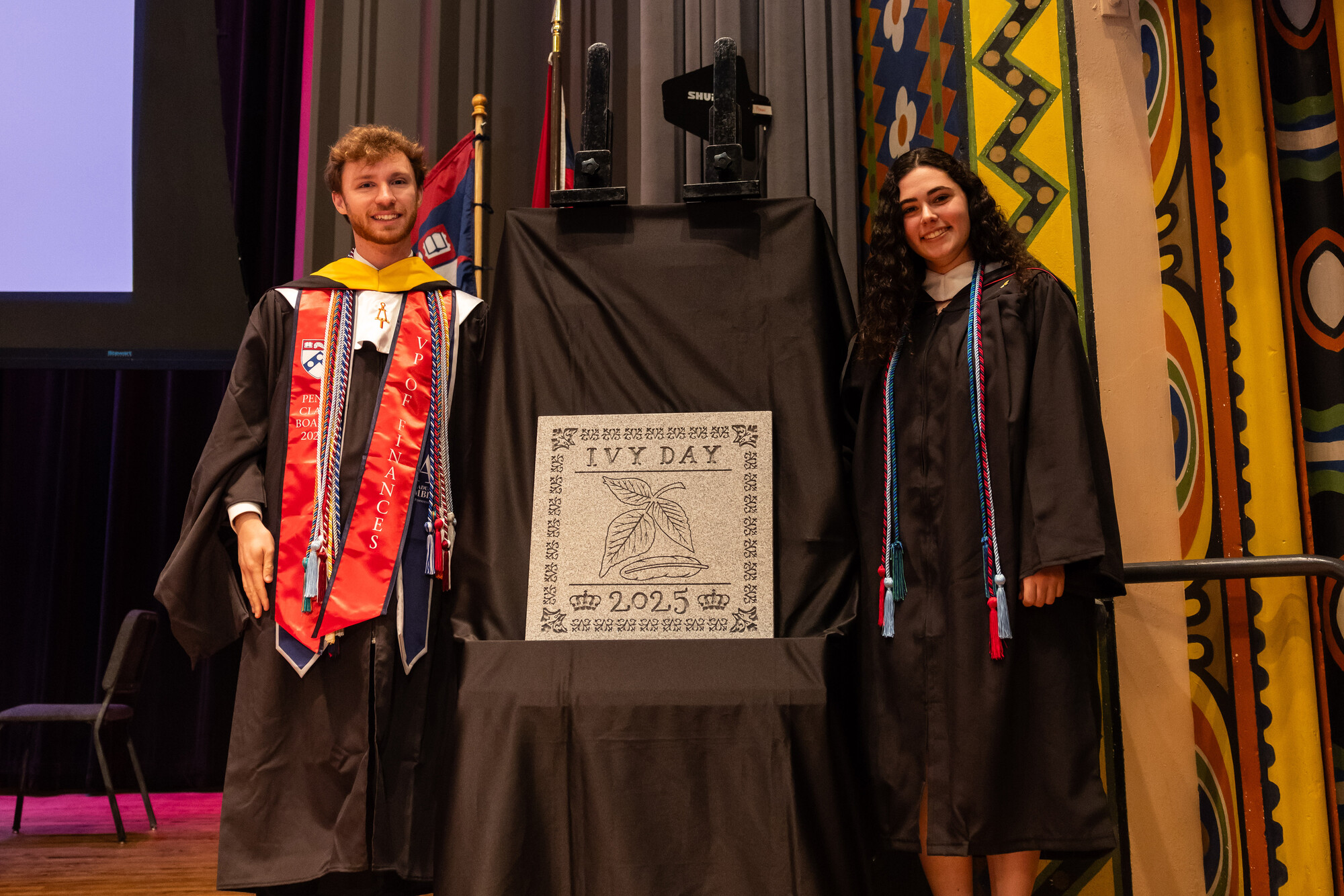 Two students next to the revealed Ivy Day Stone at Penn’s Baccalaureate celebration.