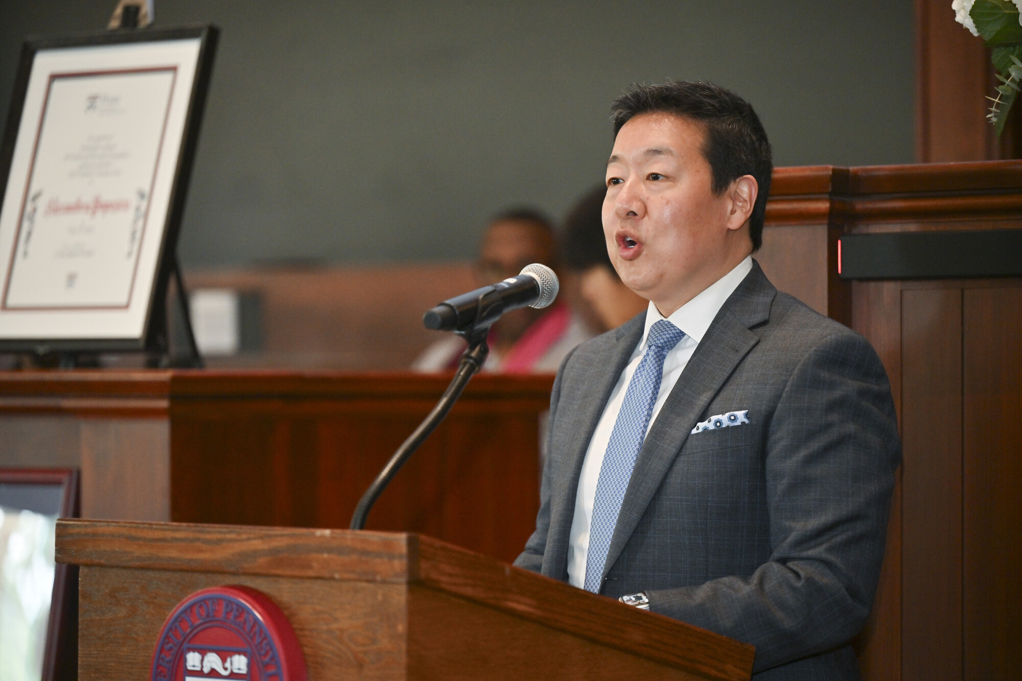 Karu Kozuma speaking at a podium at Penn’s Ivy Day Ceremony.