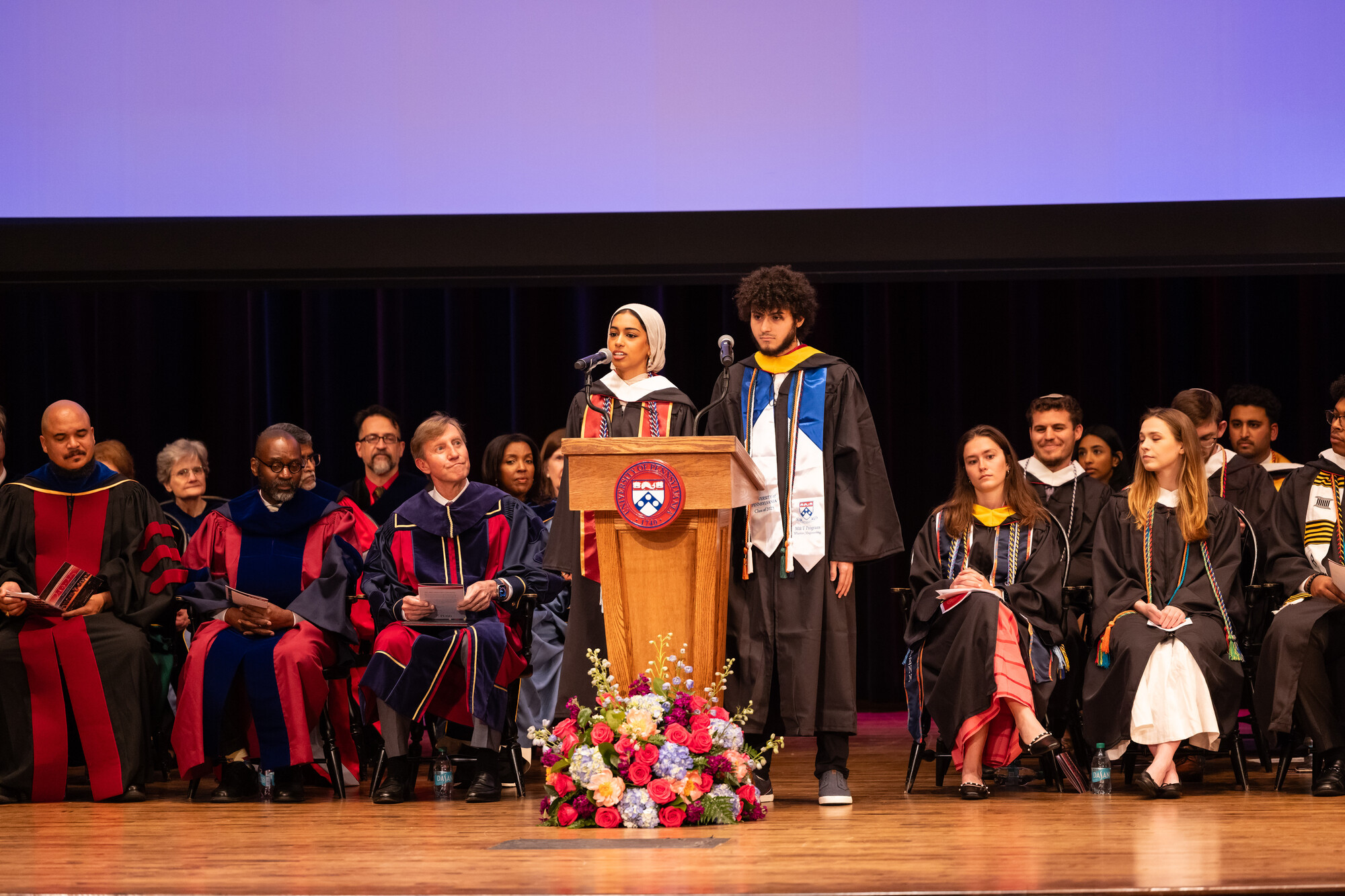 Two students speaking at a the podium at Penn’s Baccalaureate ceremony.