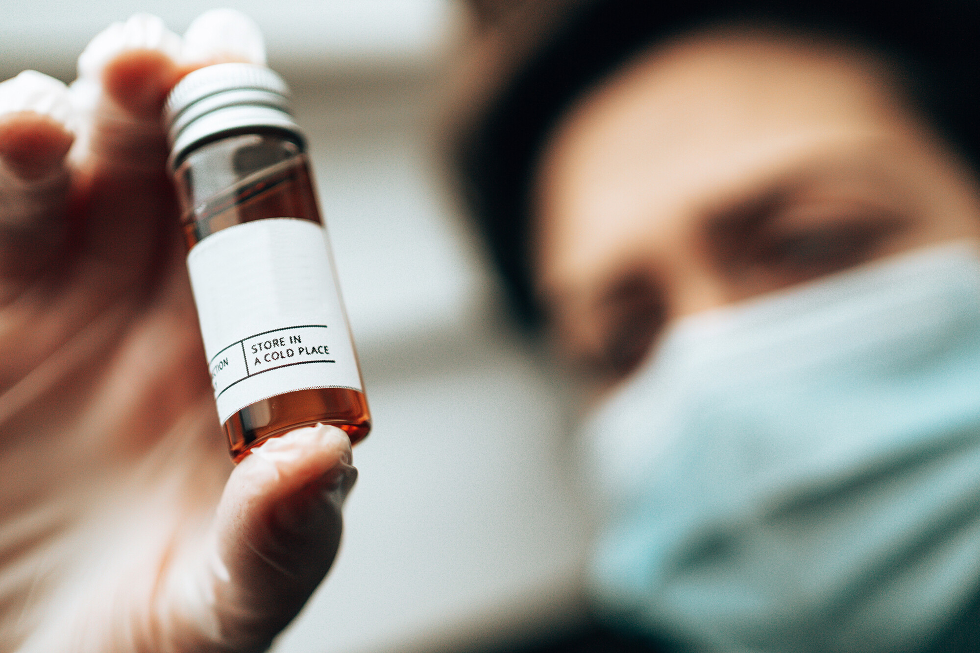 Person in mask holding vaccine vial.