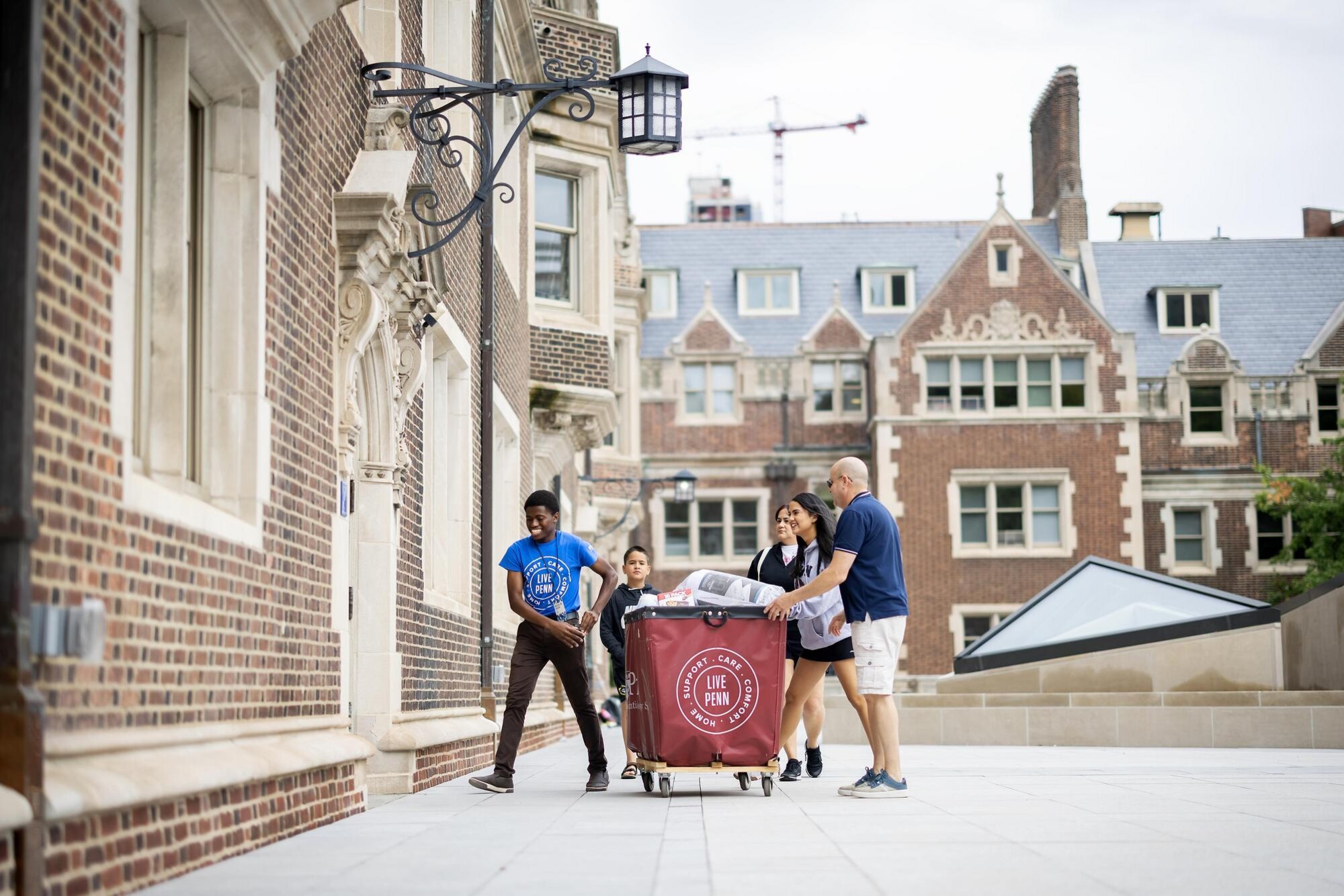 A Move-In volunteer helps a family pushing a Move-In cart into a dorm in Penn’s Quadrangle.