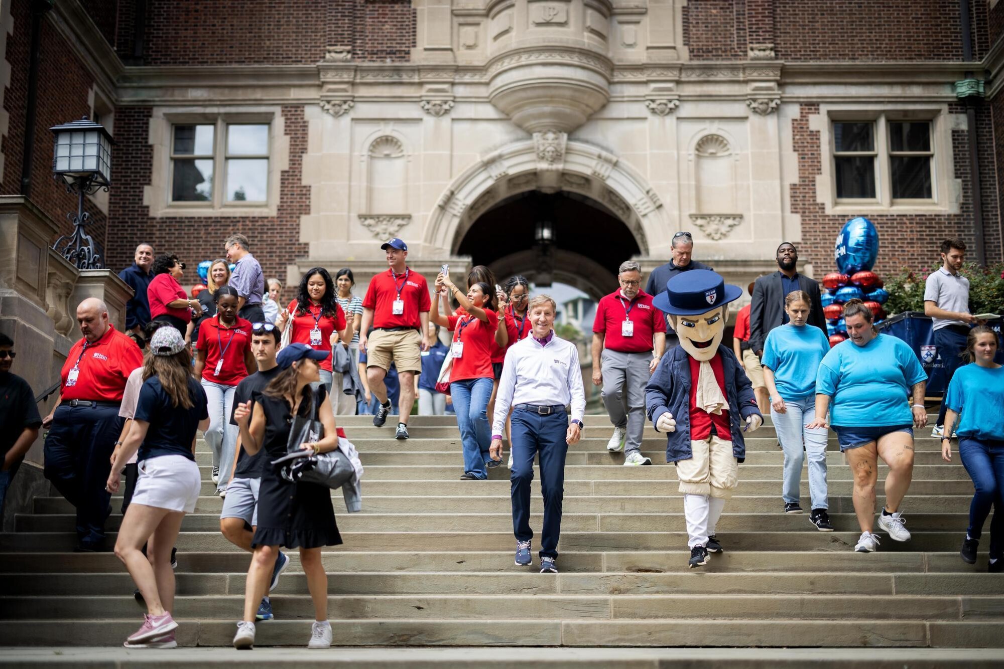Penn President J. Larry Jameson descending stairs on Penn’s campus next to the Quaker mascot and many others on Move-In Day.