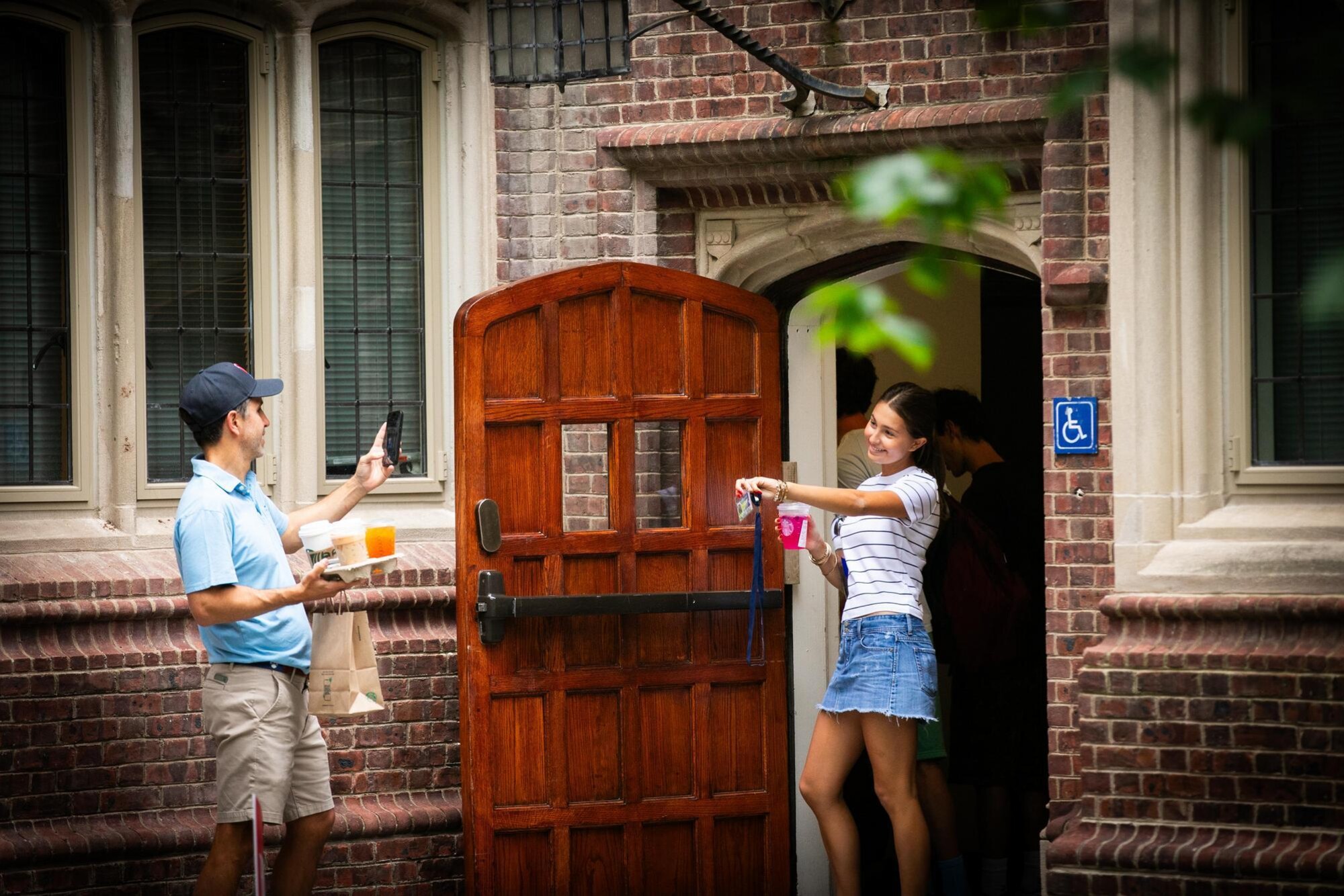 A parent takes a picture of their new Penn student holding up their Penn card in front of a College House.