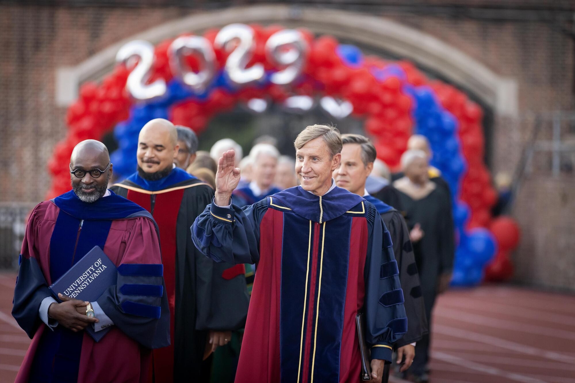 Chaz Howard, John L. Jackson Jr., J. Larry Jameson and others in convocation regalia wave as they walk onto Franklin Field for Penn’s Convocation.