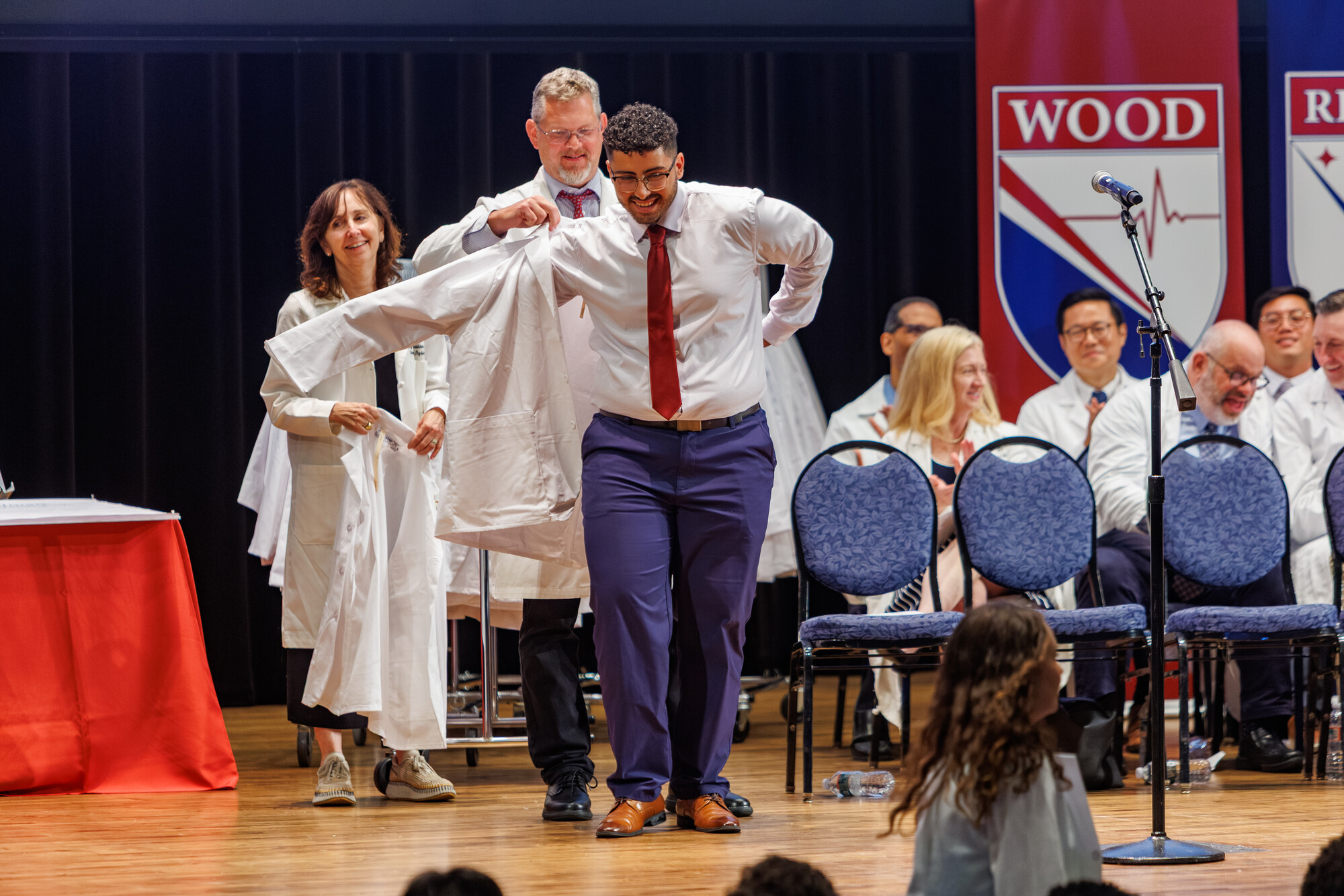 A student having their white coat put on by a doctor on stage at Penn’s White Coat ceremony.