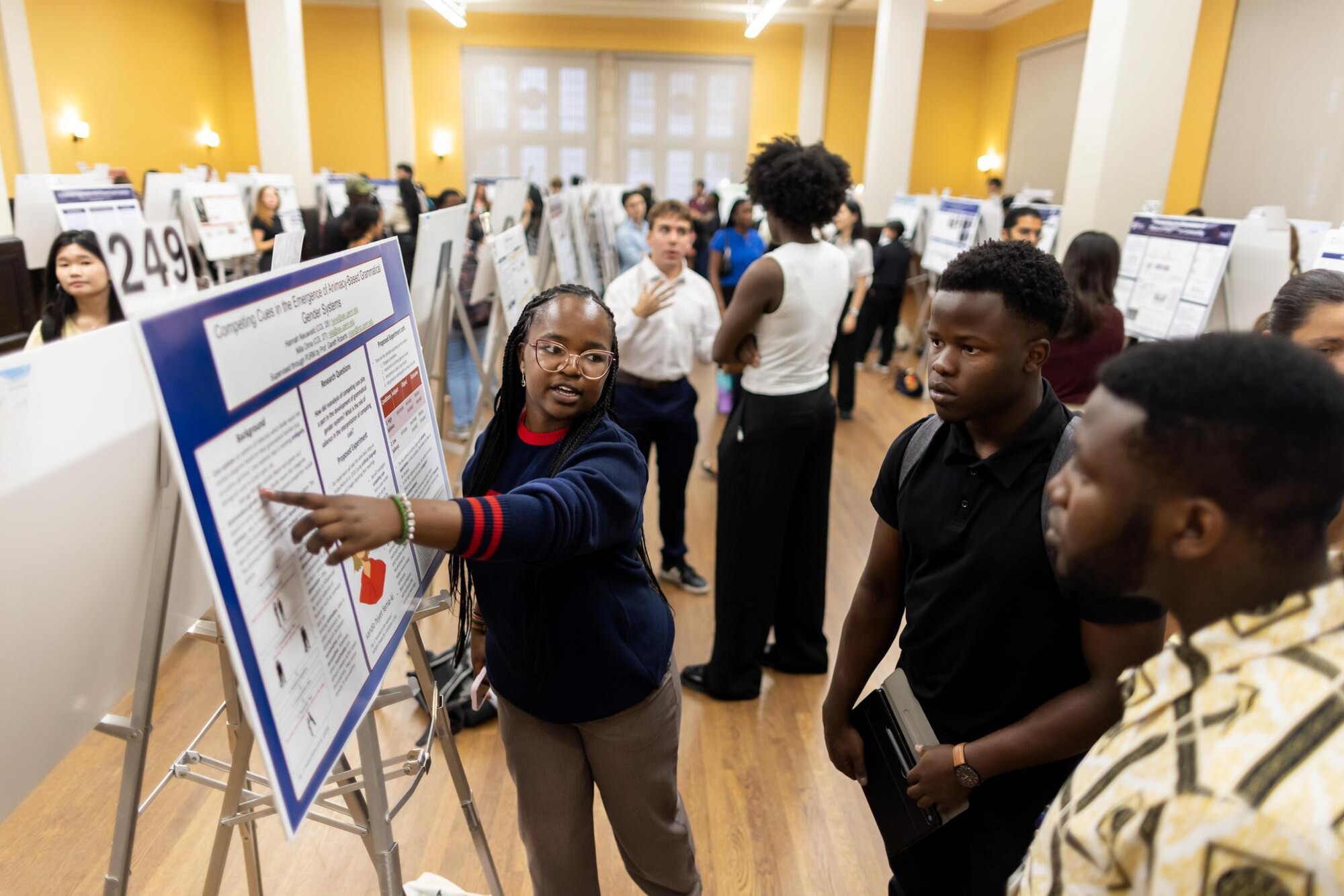 A student shows their CURF poster to visitors at Houston Hall’s CURF Poster Expo