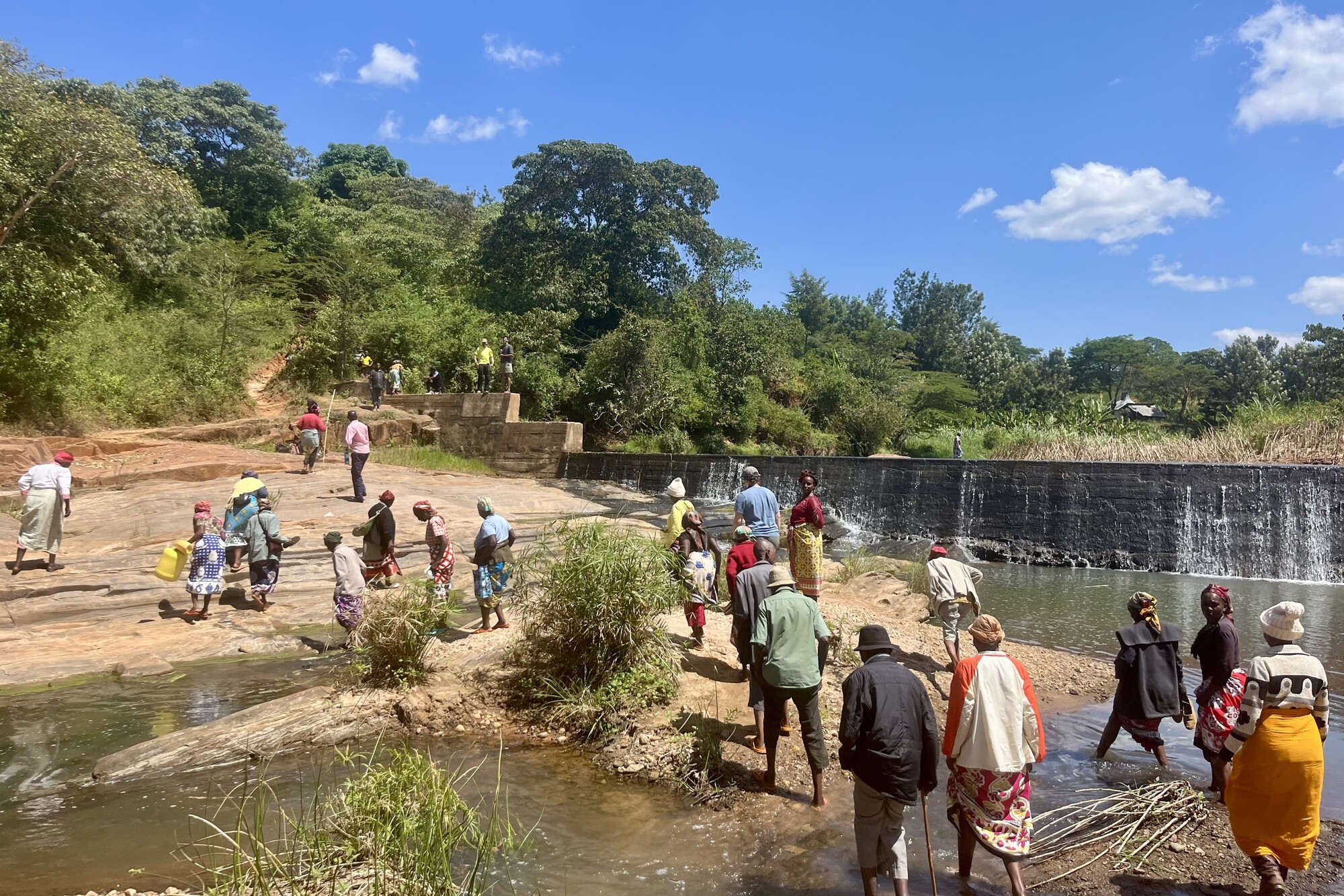 People walking along a river near a dam in Kenya.