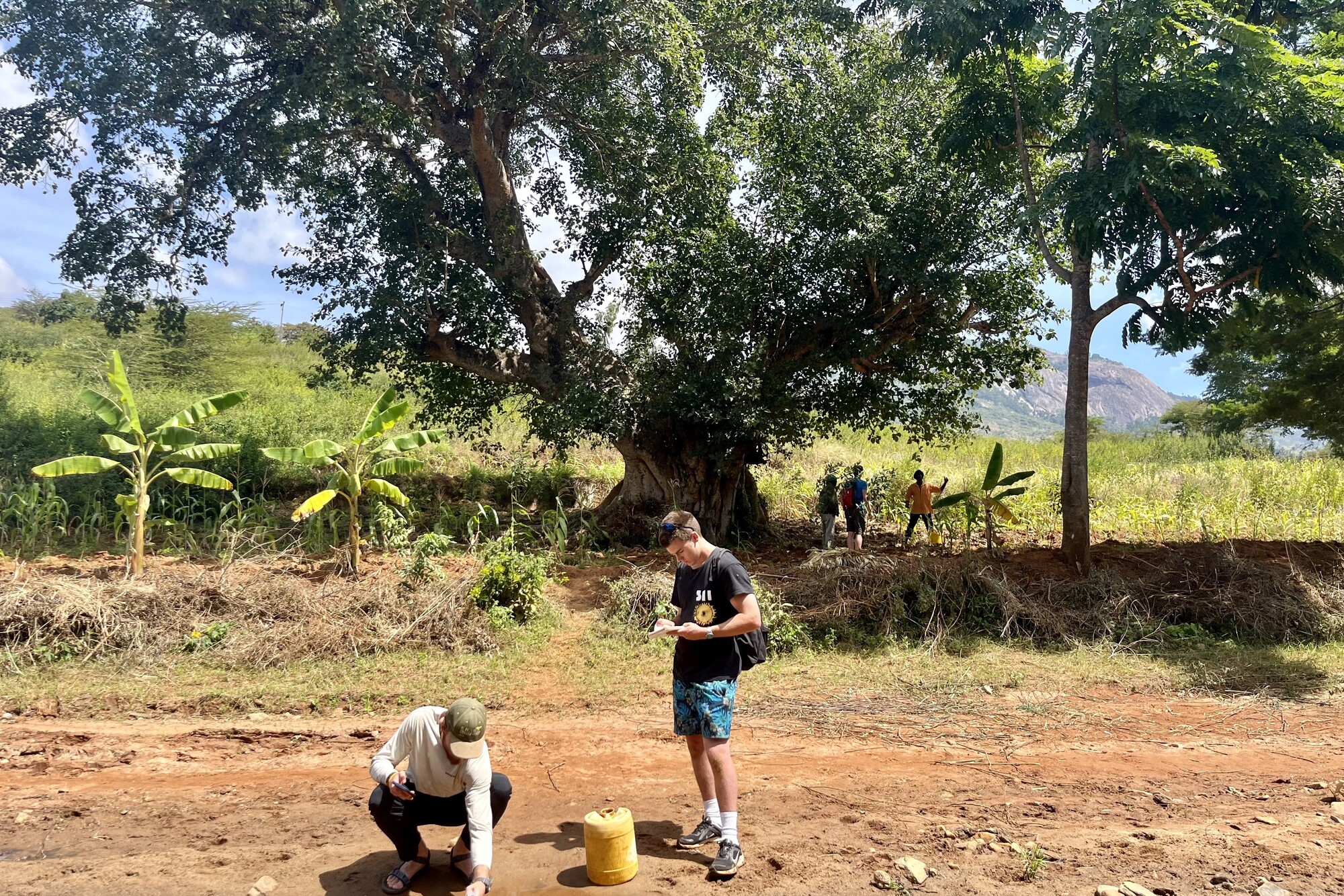 Two people at a riverbank in Kenya doing land research.