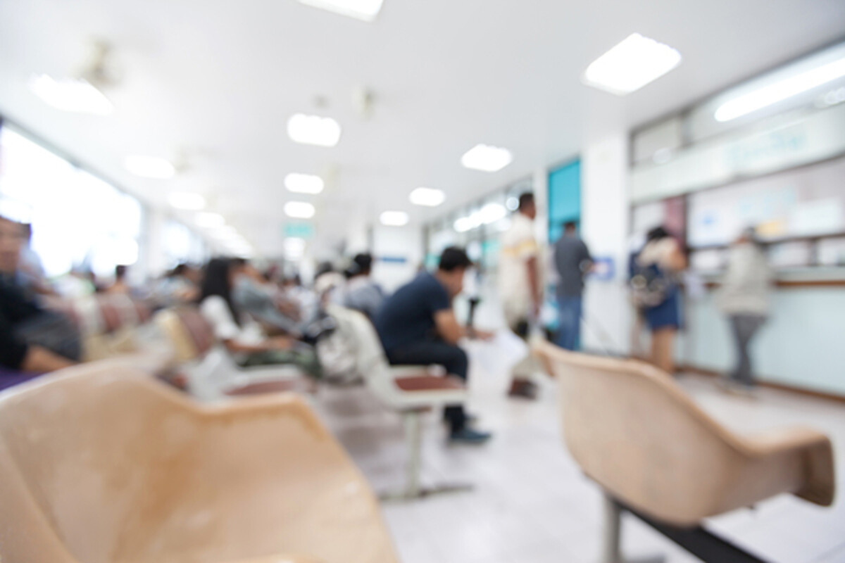 Burred image of empty chairs in foreground and a crowded medical waiting room in background