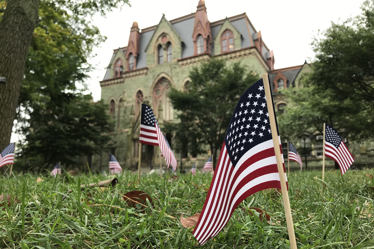 Many small flags placed in the grass on College Green in front of College Hall.