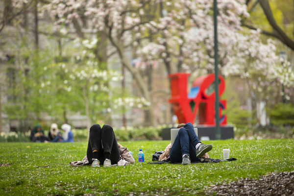 2 students laying on grass in front of Robert Indiana’s LOVE statue on Penn’s campus.