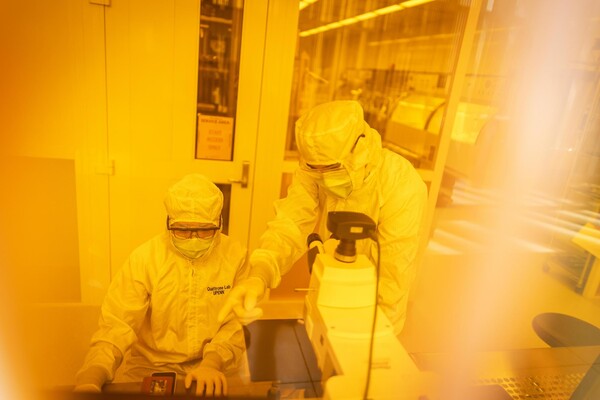 Researchers in a clean room pointing at a microscope.