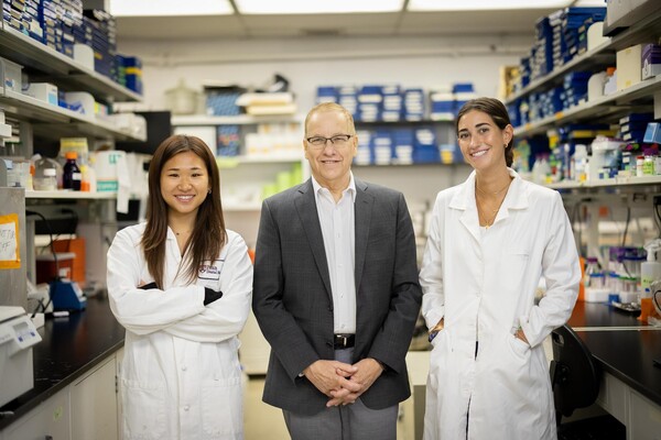 Two students in lab coats surround a professor in a suit. 